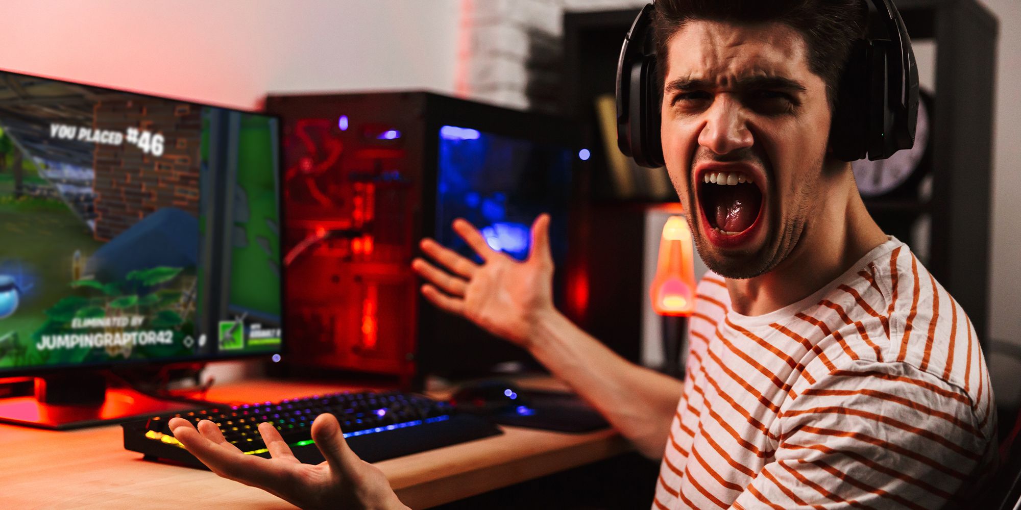 a male gamer sat at a desk shouting angrily while holding a hand up to the scream