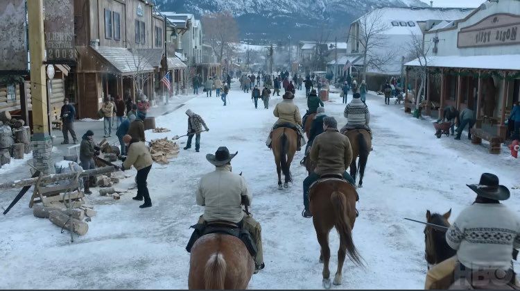 An image showing horsemen, people, and wooden buildings in a settlement in Wyoming from The Last of Us episode 6