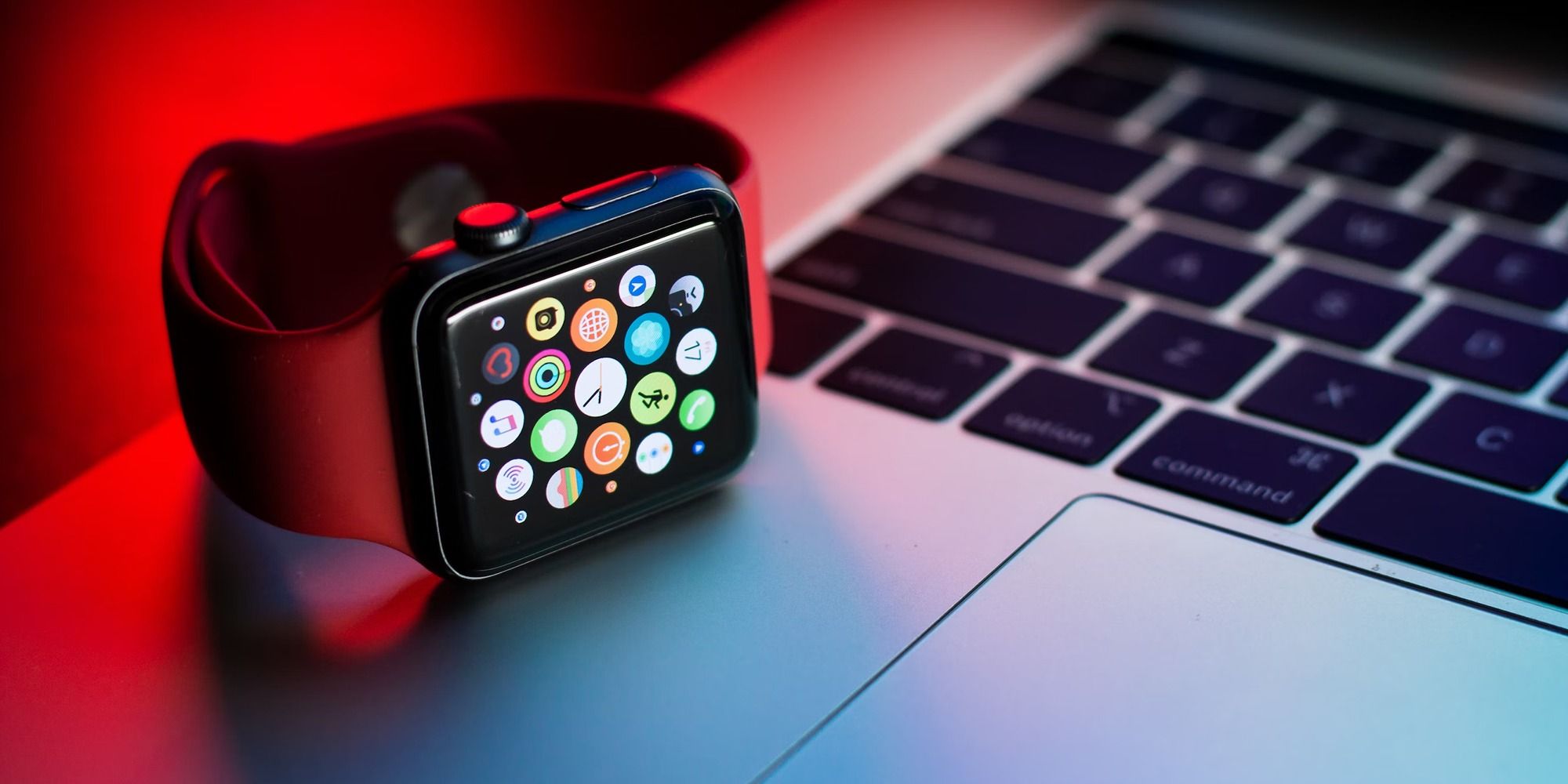Photo of an Apple Watch on top of an Apple laptop, with a red light in the background creating a mood.
