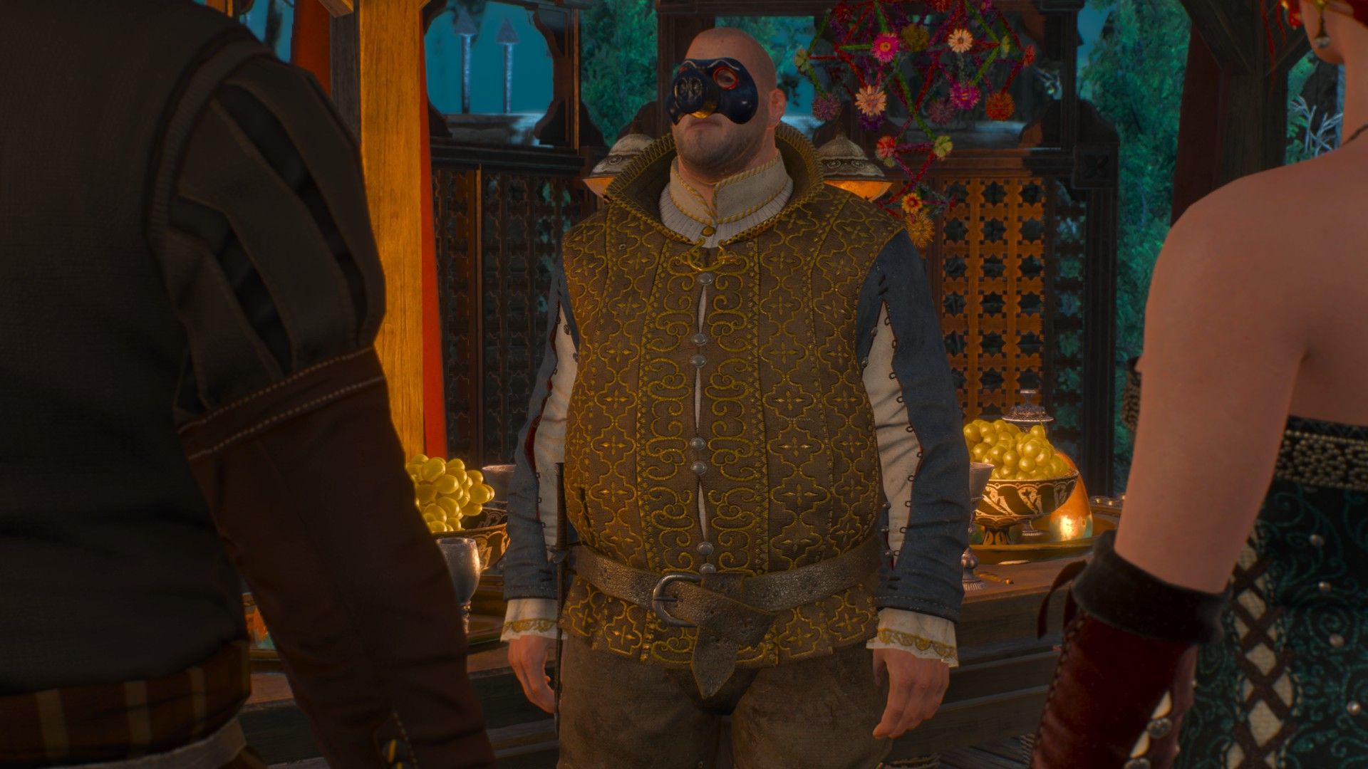 Sigi Reuven, wearing a pig mask, talks to Geralt and Triss at a ball.  They are standing next to a buffet table overflowing with food.