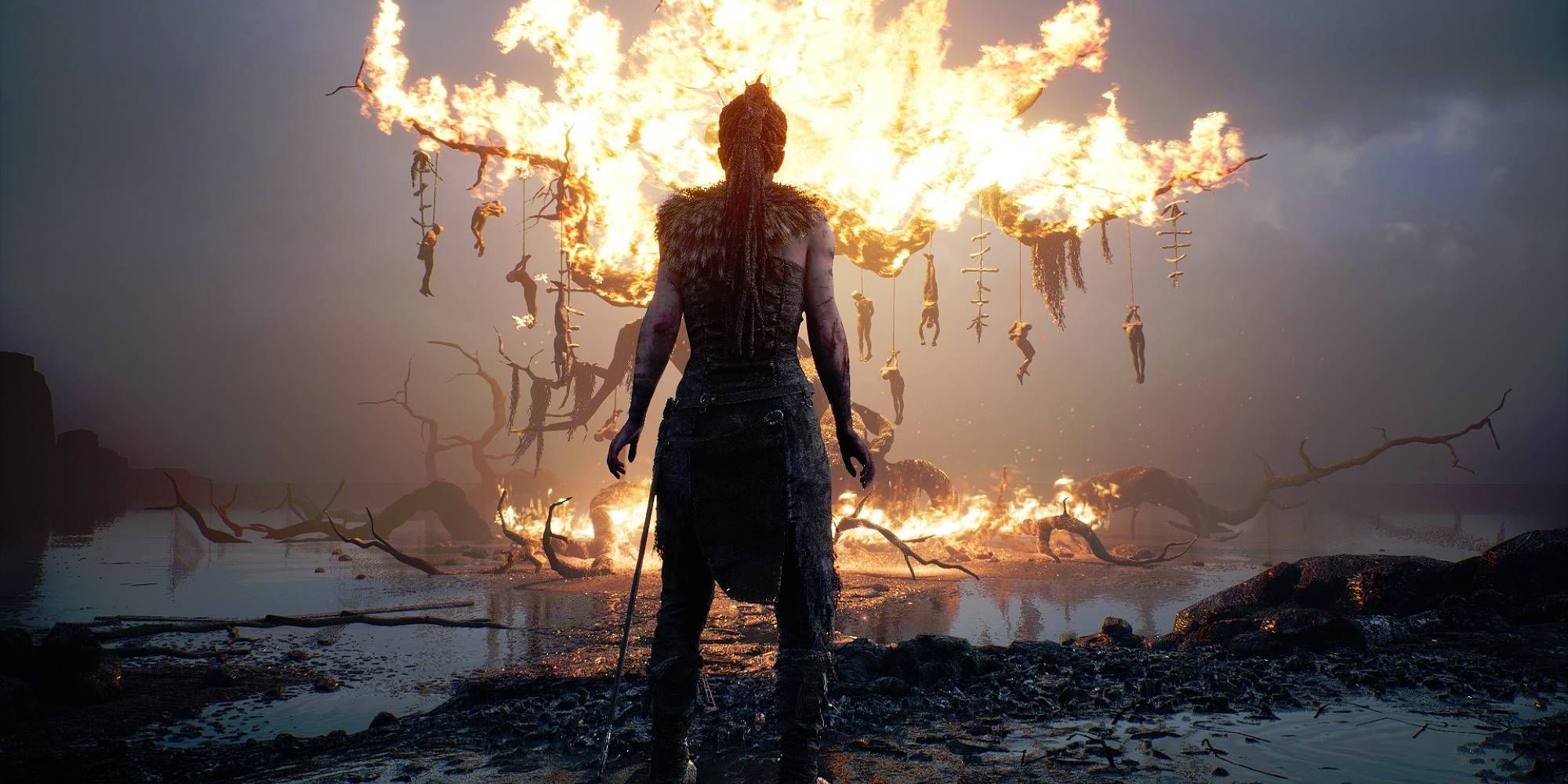 A woman stands in front of a burning tree on a dying landscape