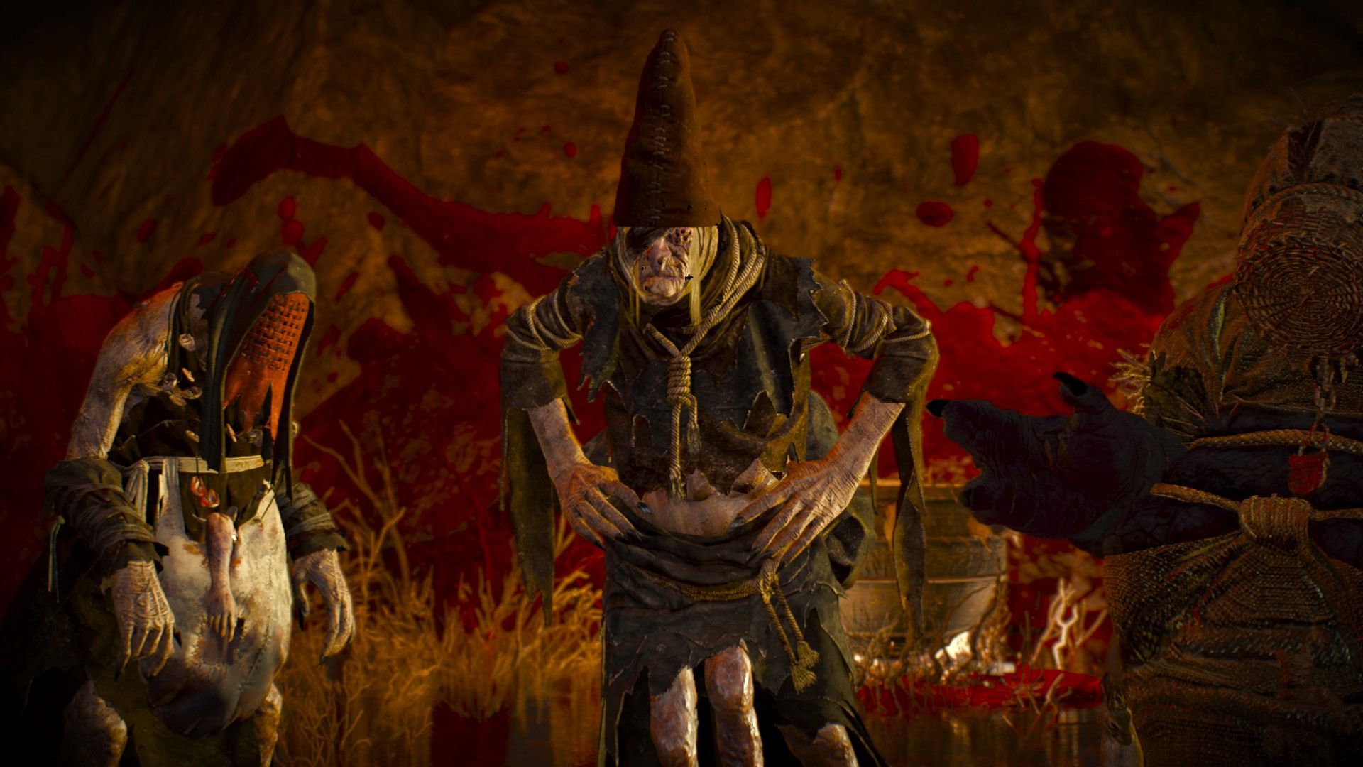 A trio of monstrously deformed women gather in a cave covered in blood.