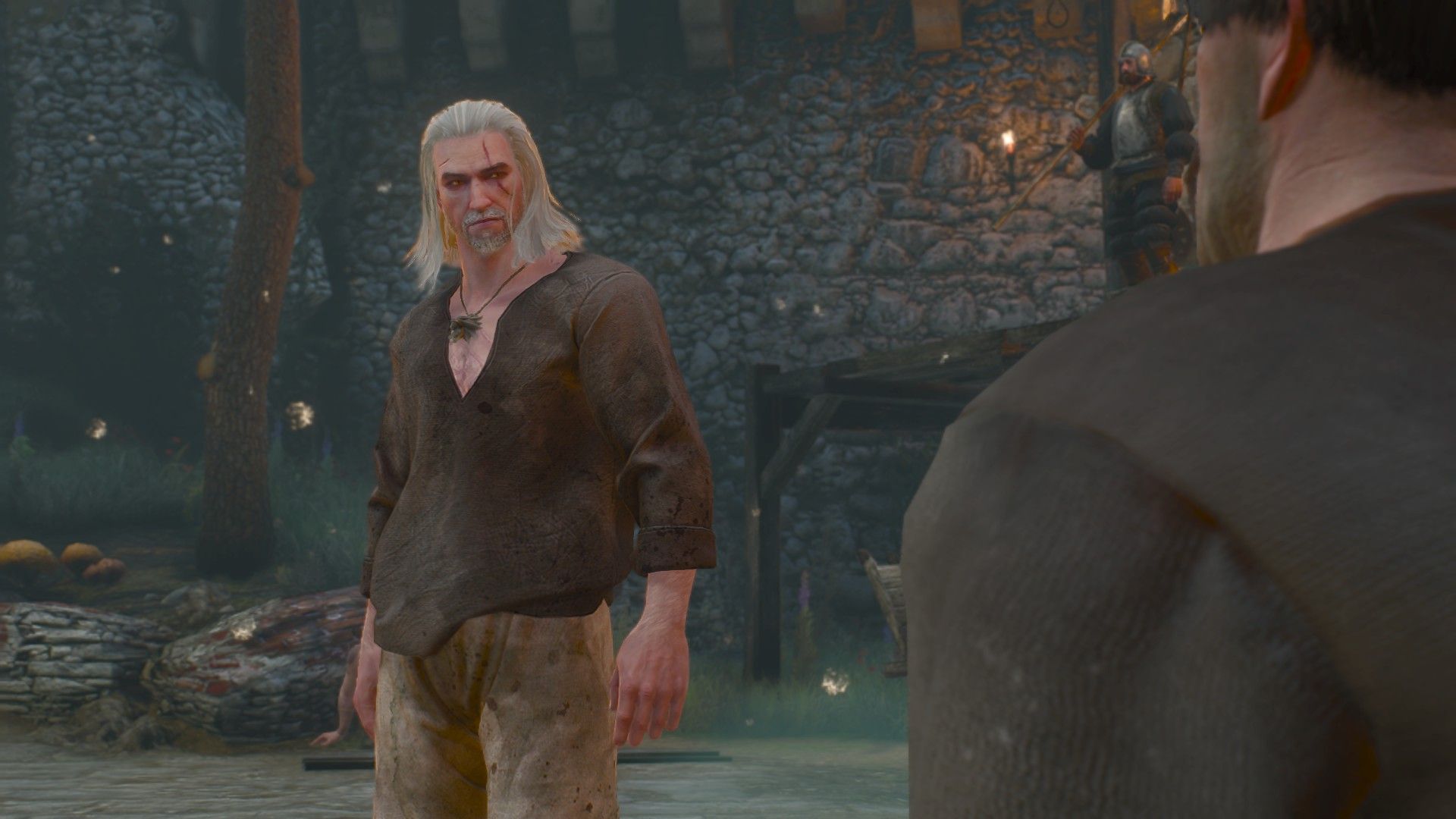 Geralt, dressed in prisoner&rsquo;s clothes, talks to a fellow prisoner in a castle.