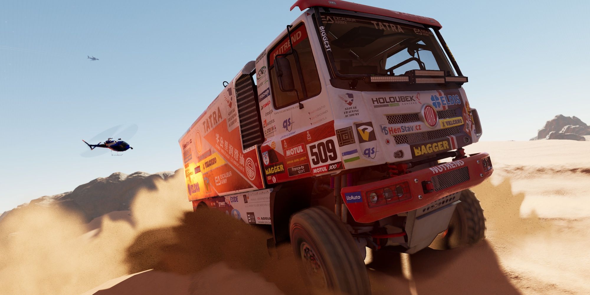 Dakar Desert Rally: A Sand Truck Crossing A Dune Whilst A Chase Copter Follows