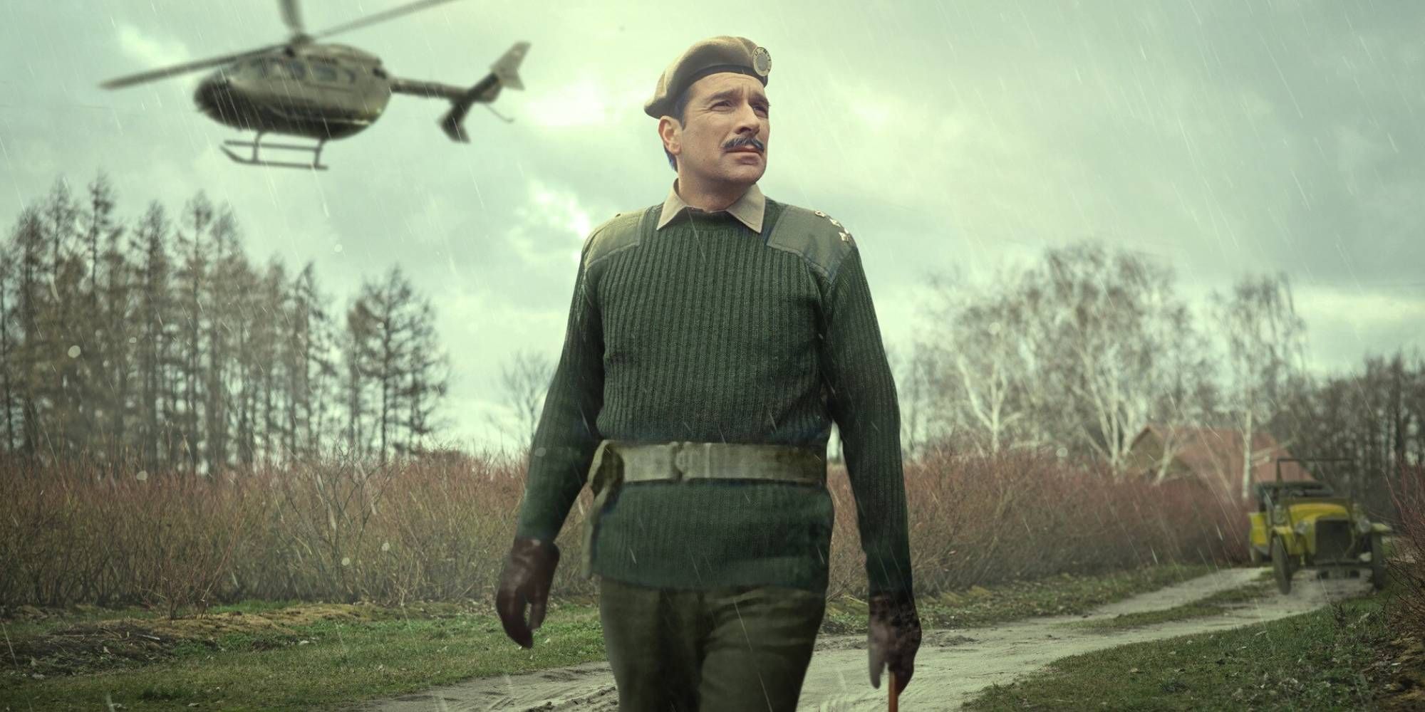 A man in a green military vest whilst a helicopter flies in the background