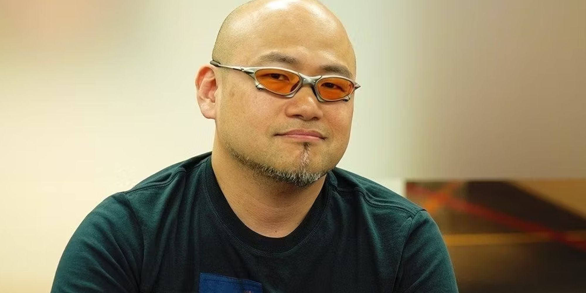 hideki  sitting in front of a cream-coloured wall with orange sunglasses