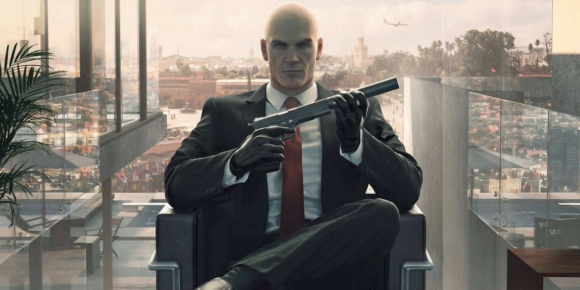 Agent 47 sat down as he screws a suppressor onto a pistol.