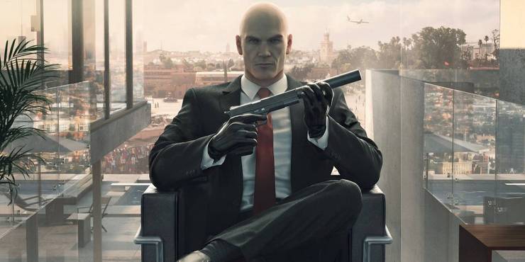 Agent 47 sat down as he screws a suppressor onto a pistol