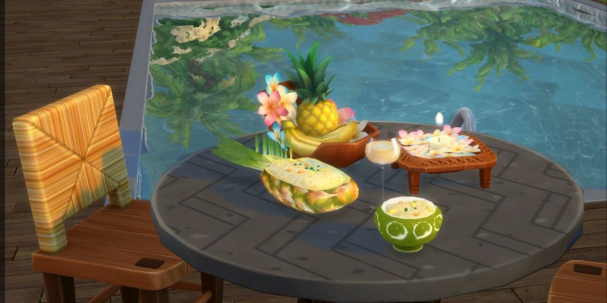 Screenshot of The Sims 4 showing a table and chair outdoors near a swimming pool. On the table sits a bowl of pineapple fried rice, a hollowed out pineapple full of fried rice, a cocktail, a bowl of fruit, and some tropical flowers.