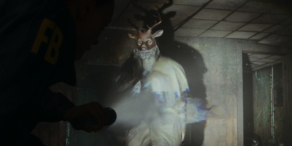 a Taken cultist in a deer mask illuminated by a flashlight in Alan Wake 2