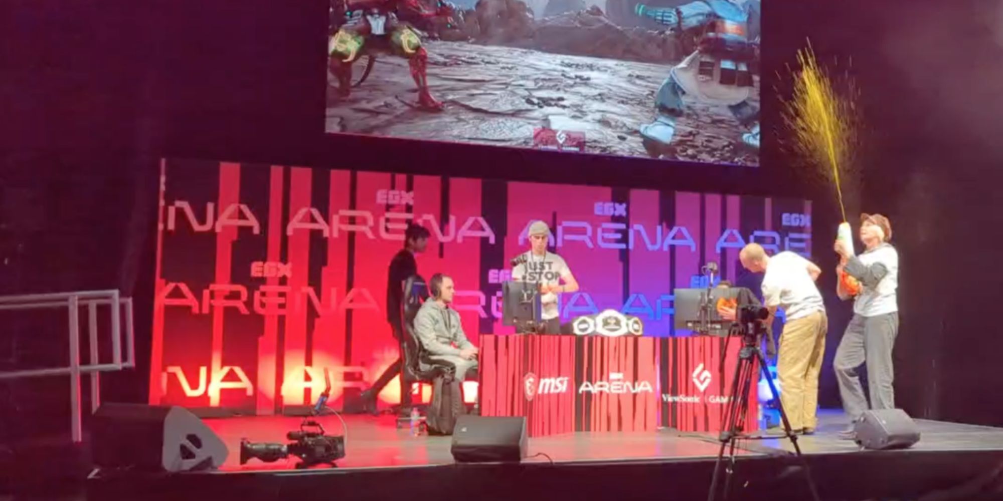 Members of Just Stop Oil protest EGX by walking on stage during a Tekken 7 tournament. Two members smear paint of computer monitors, while another fires paint from a water gun