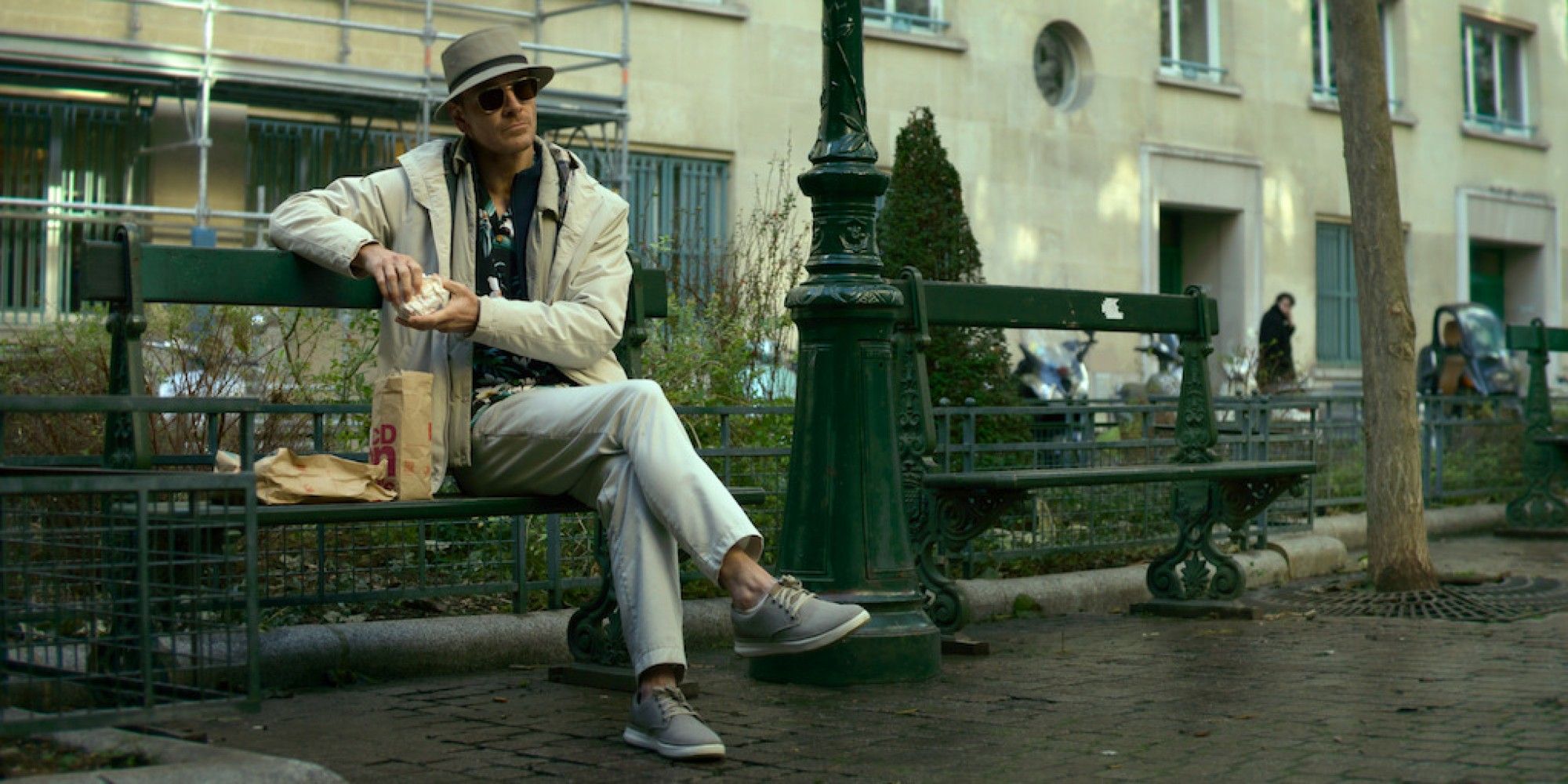 Michael Fassbender in The Killer eating McDonald's on a park bench in Paris