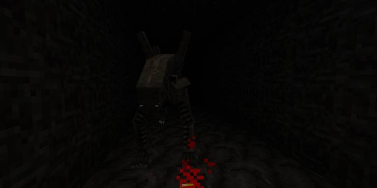 A first-person view of a dark, narrow corridor with a black-skinned alien approaching.