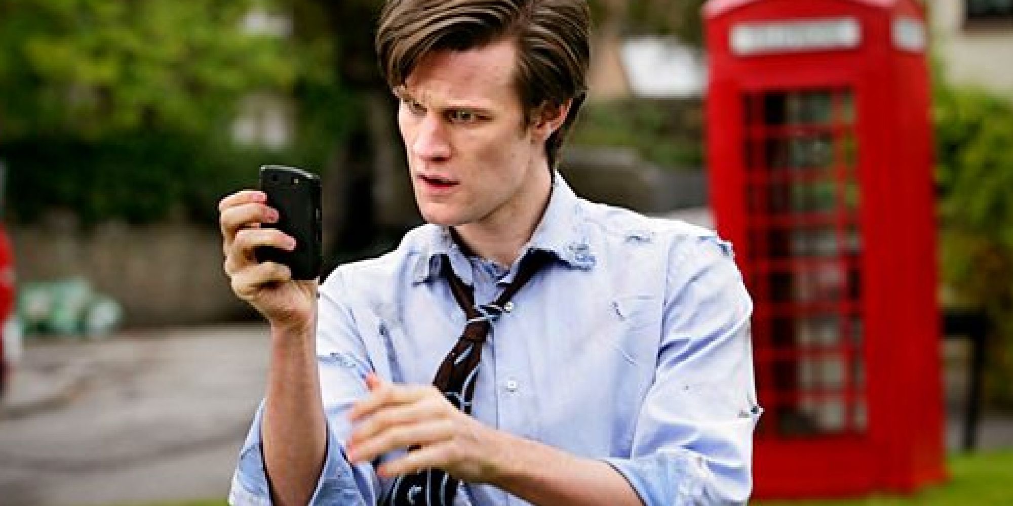 The 11th Doctor in the 10th Doctor's tattered clothes inspecting a mobile phone in front of a red phone box in Doctor Who's The Eleventh Hour
