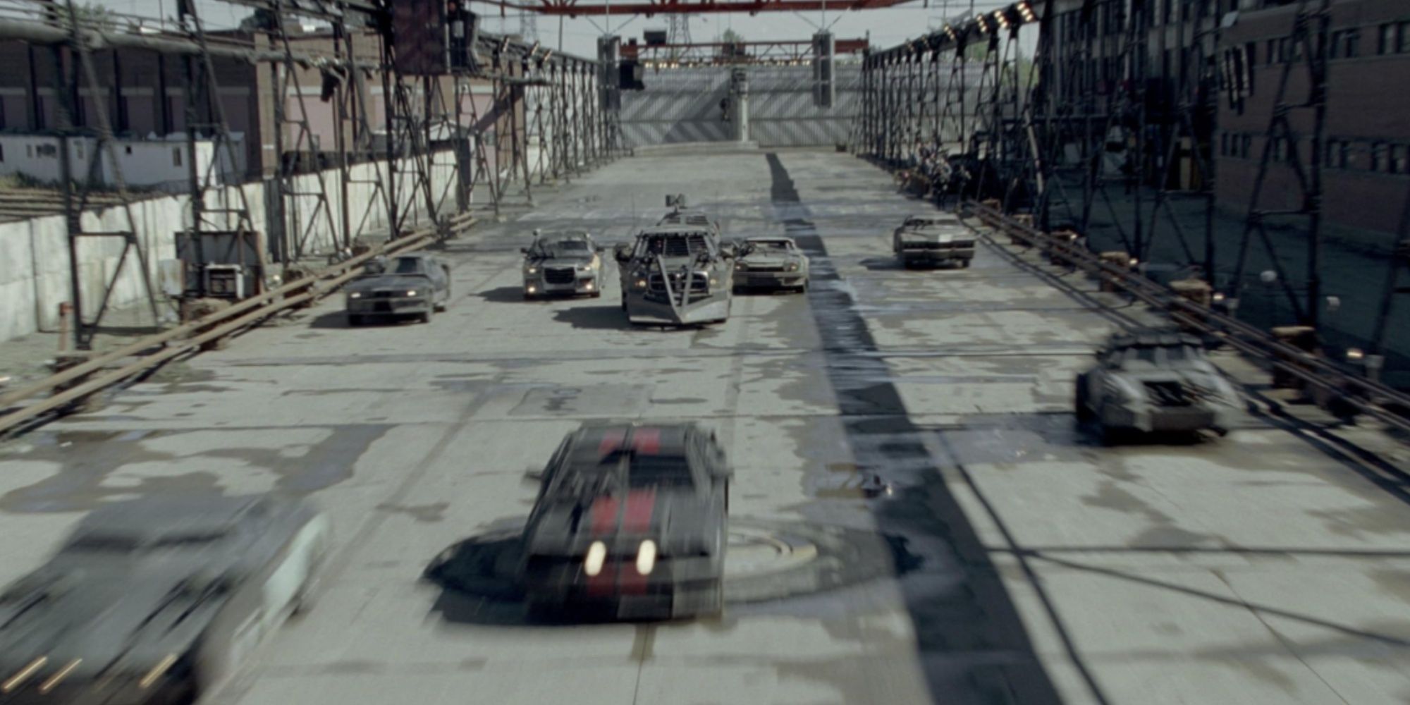A series of cars competing in the prison's Death Race, with the car leading in front driving over a weapons system button.
