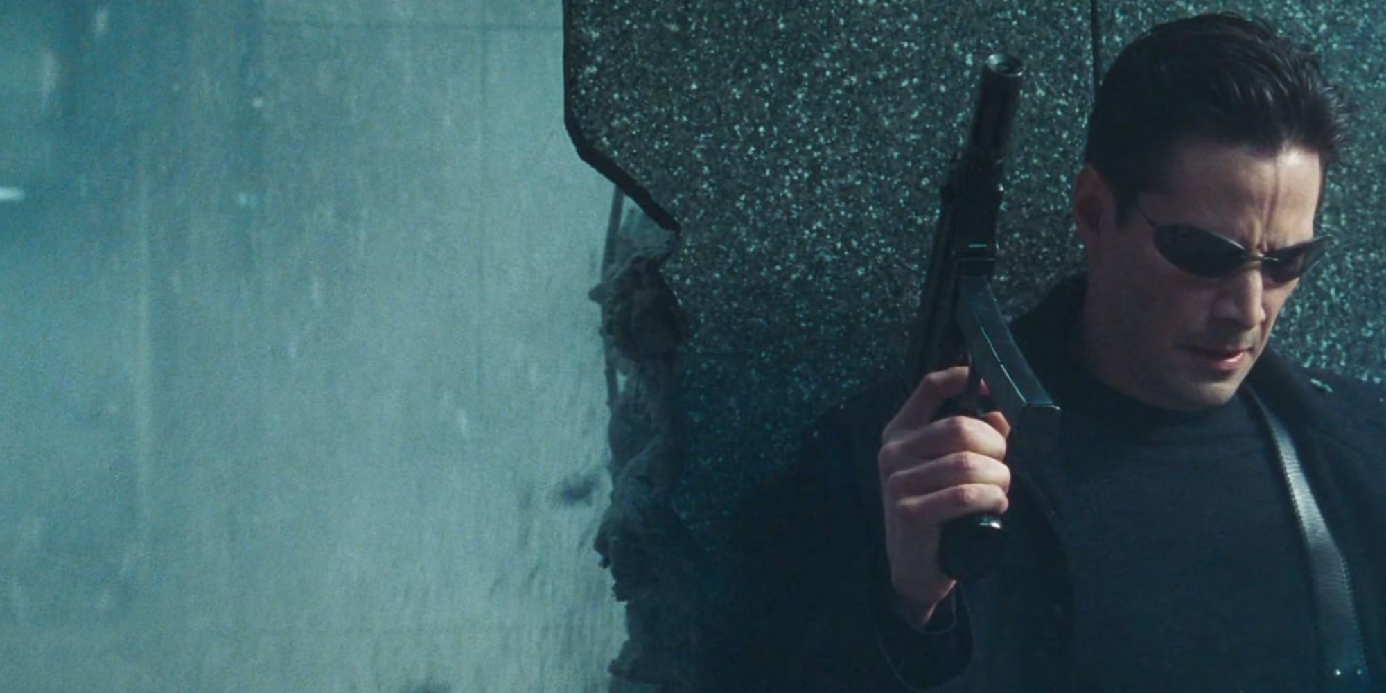 Keanu Reeves as Neo taking cover behind a wall that's coming apart from all the gunfire.