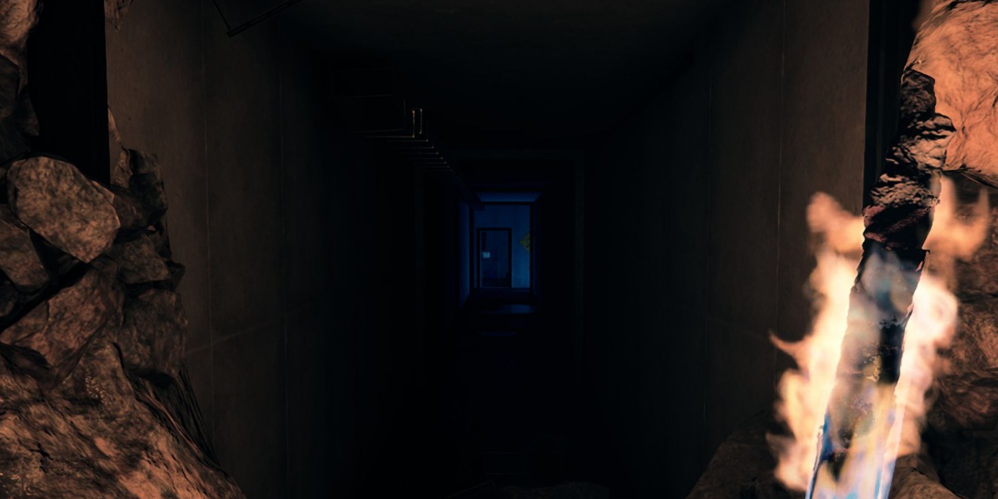 A screenshot from Sons of the Forest showing the player character holding a lit torch while staring down a long and dark hallway at the end of a cave with blue light and a door at the end.