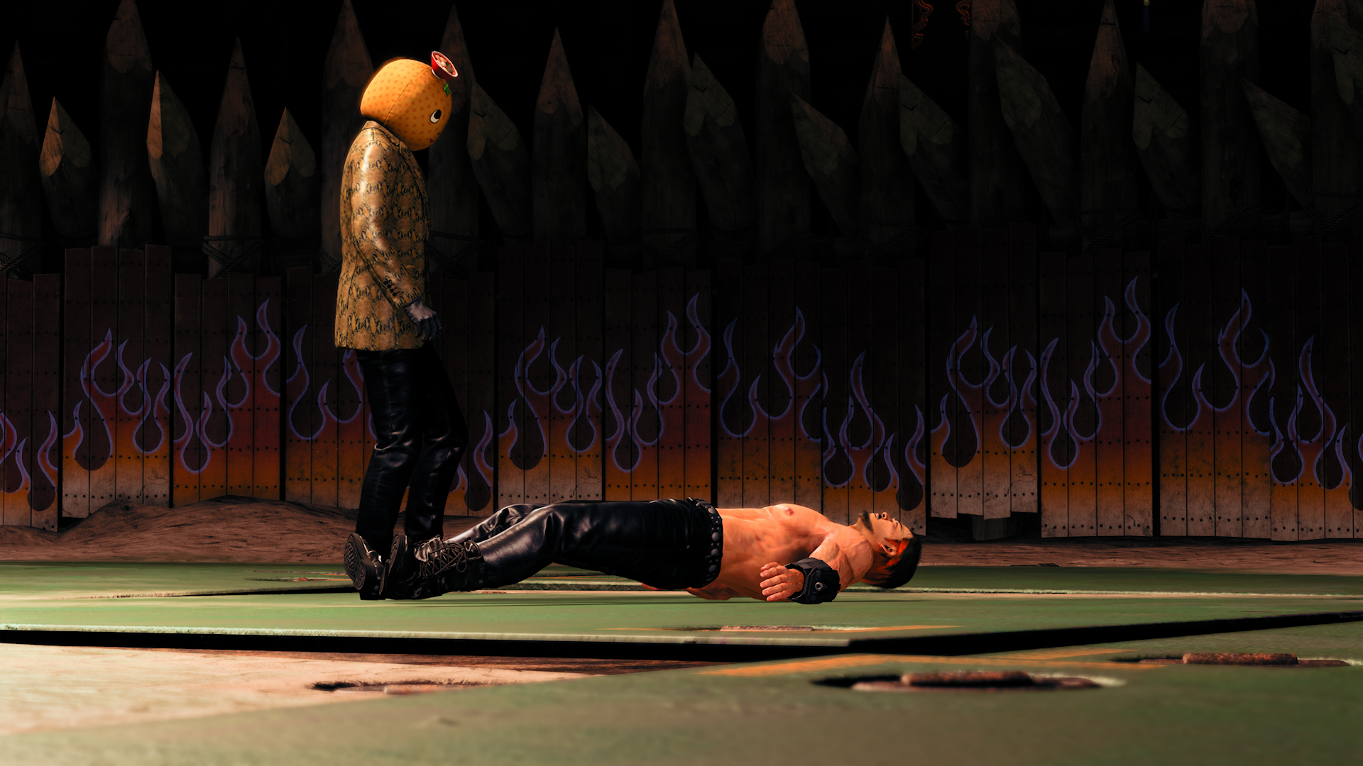 A man with a large orange costume head stands over a topless muslce man lying on the ground