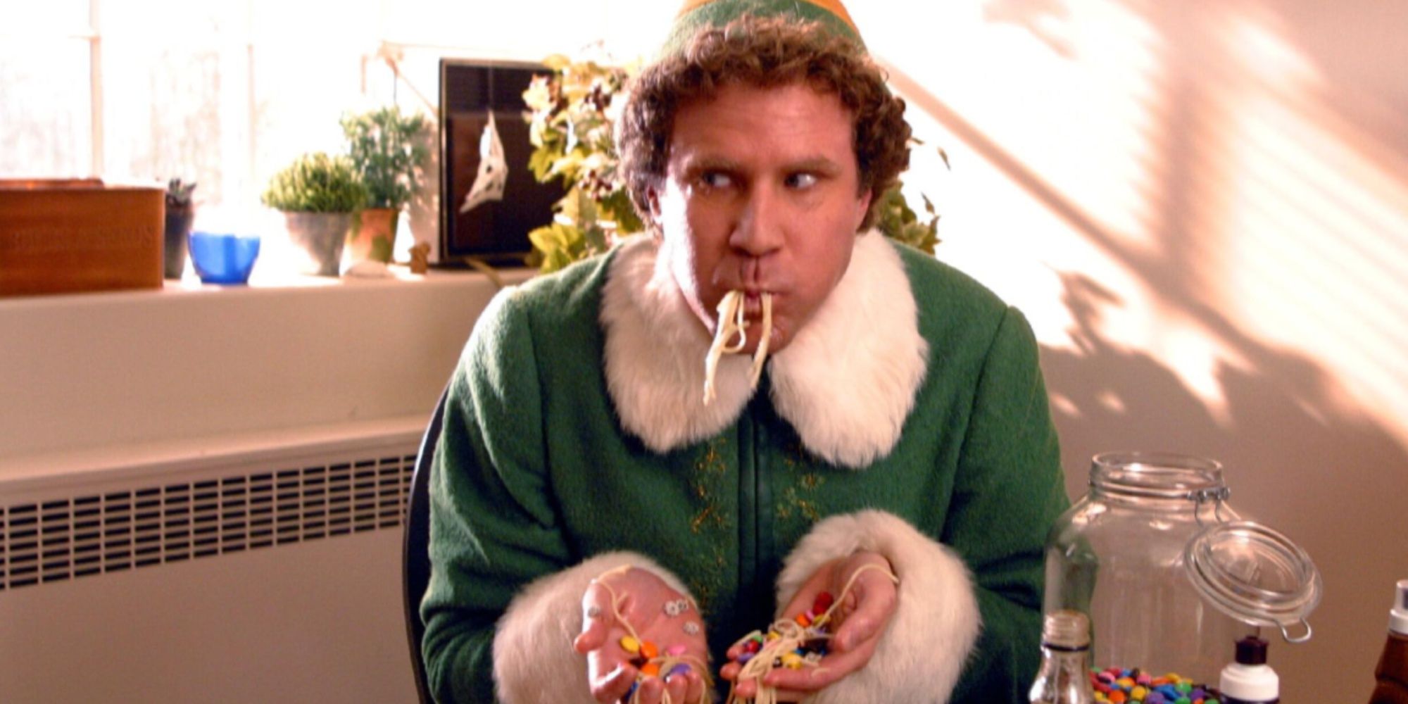 Will Ferrell's Buddy eating spaghetti with pasta and candy, an with noodles in his mouth and an open jar of M&Ms and syrups beside him.