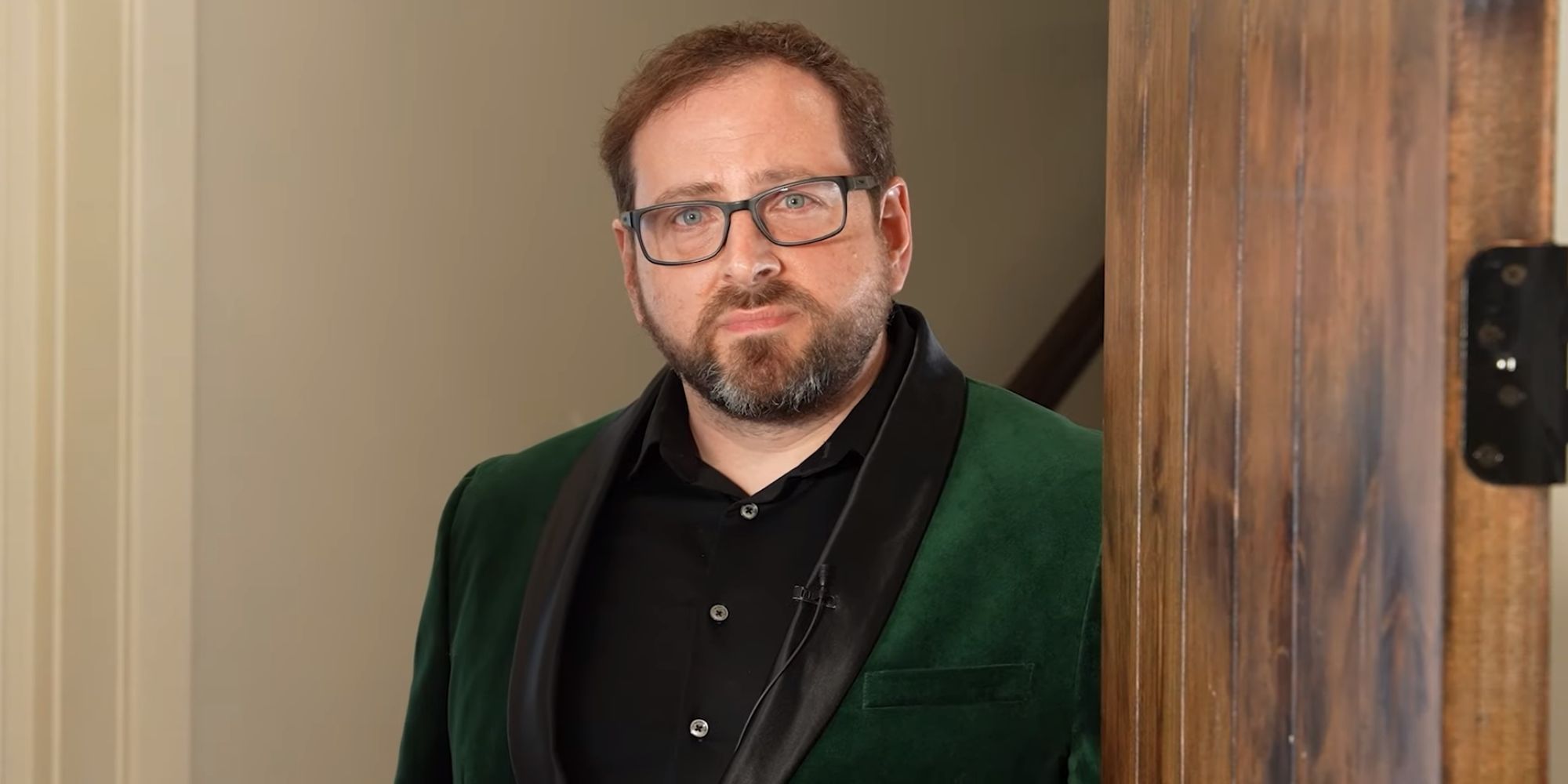 The creator of Five Nights at Freddy's, Scott Cawthon, opening the door to his home. He is wearing a green velvet suit.