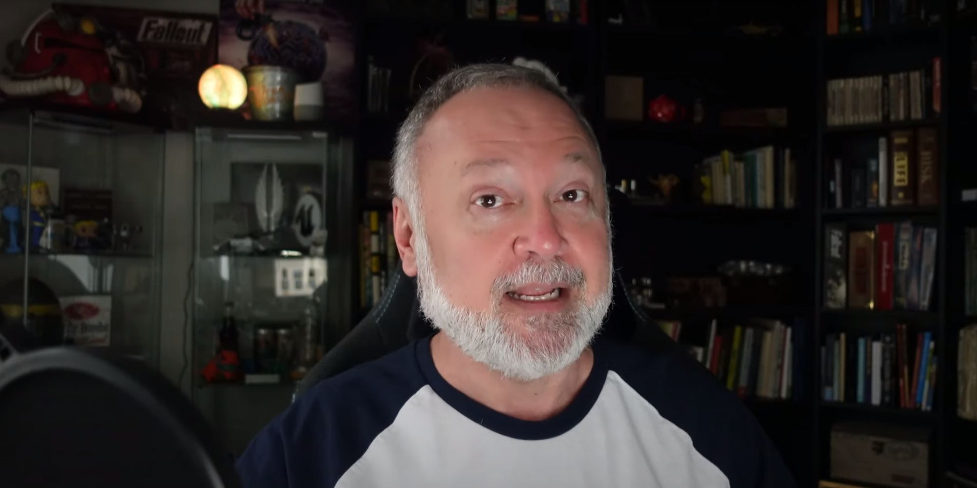 Tim Cain, the creator of the Fallout series, talking to the camera on his YouTube channel. There is merch in the background, including original Fallout merch