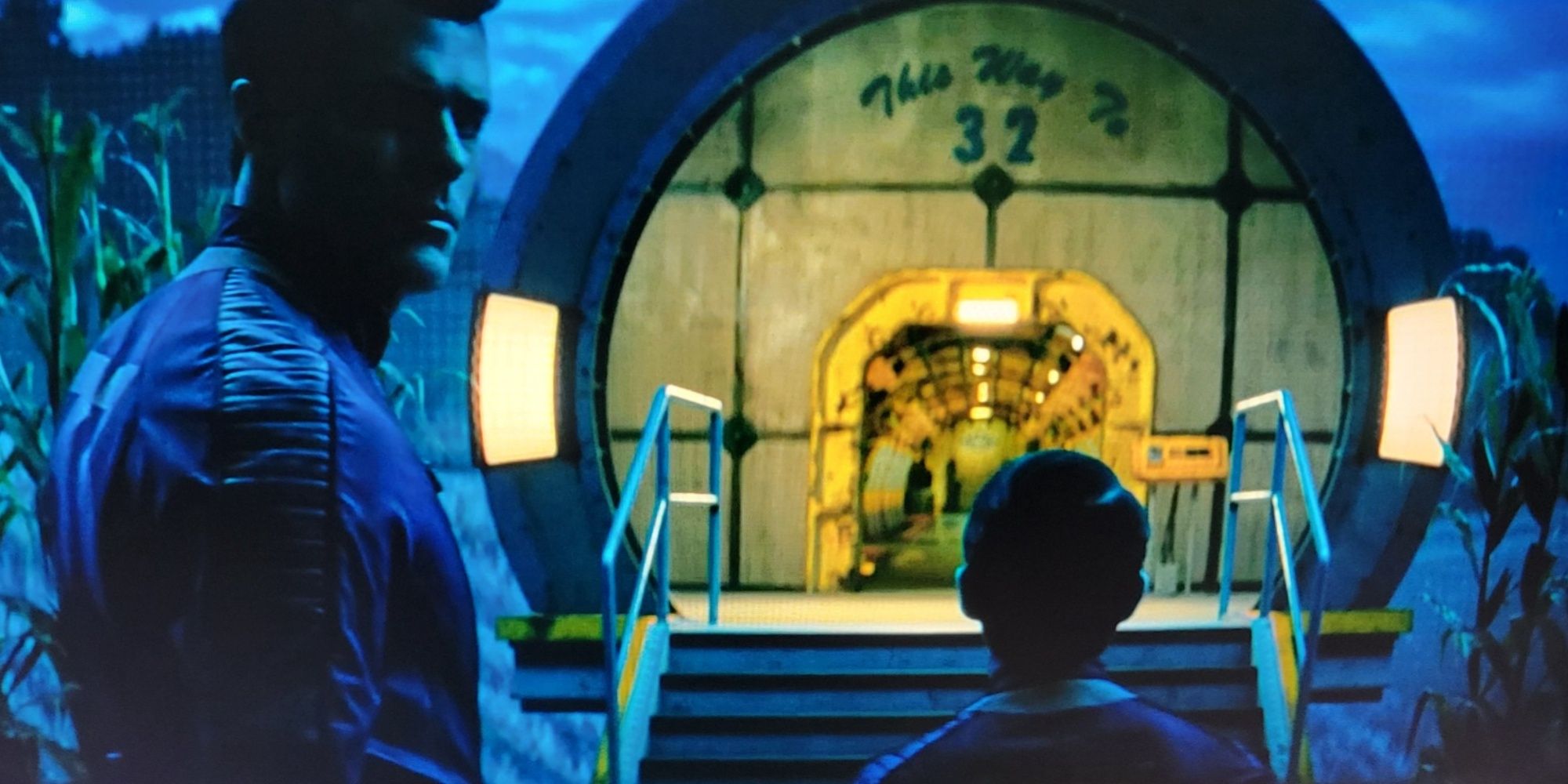 Chet facing the camera walking with his cousin Norm into the Vault 32 entryway.