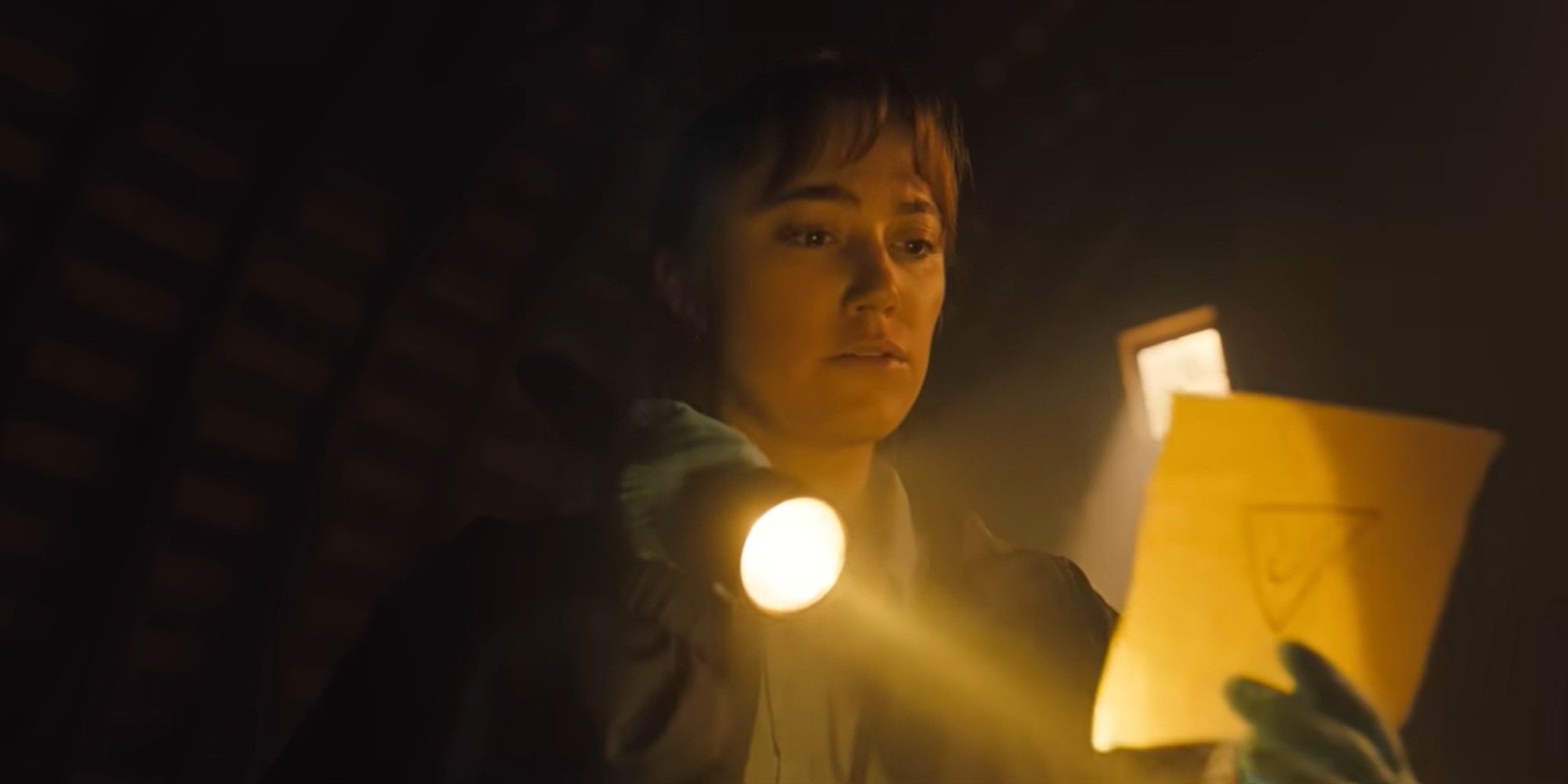 Maika Monroe as Lee Harker looks at a piece of evidence with a flashlight in Longlegs