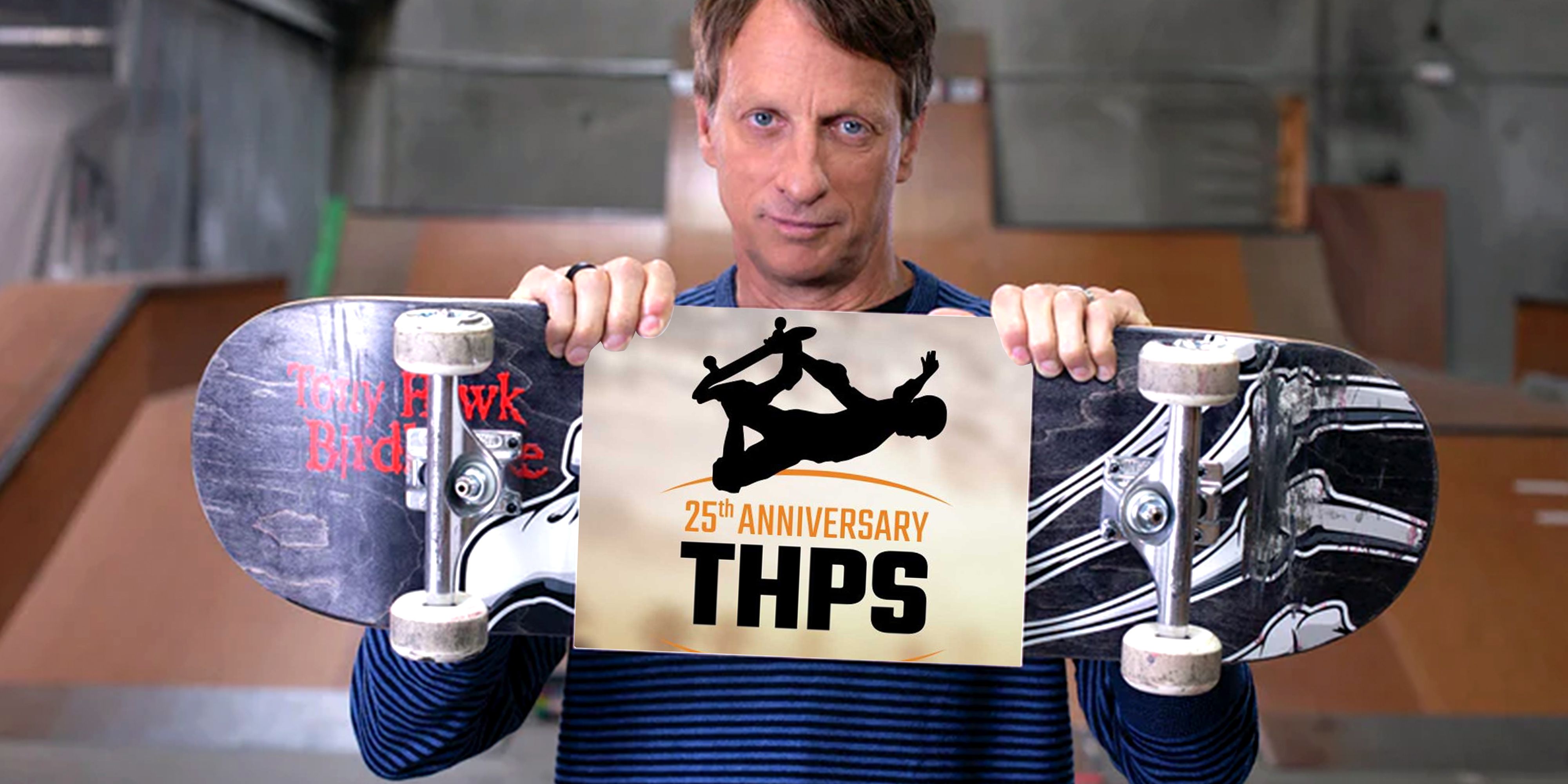 Tony Hawk holding a skateboard with a sign on it that reads '25th Anniversary THPS'