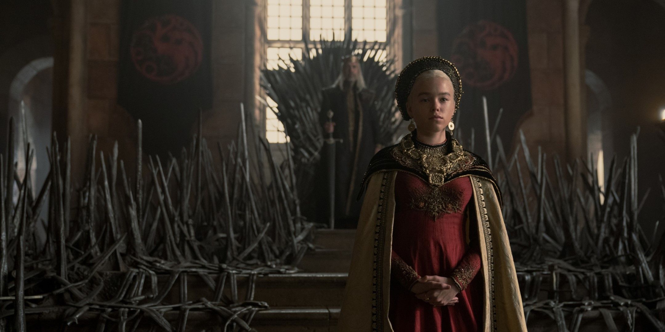 A screenshot from House of the Dragon showing Viserys and Rhaenyra standing in front of the Iron Throne.