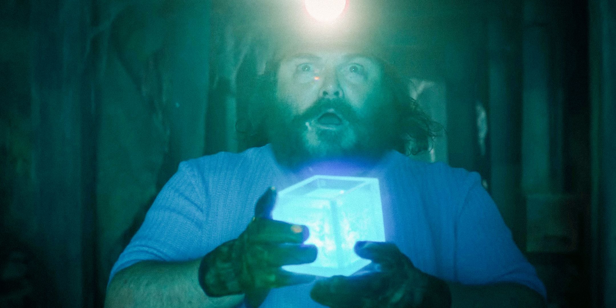 Jack Black as Steve in the Minecraft movie, holding a glowing blue cube in a mineshaft.