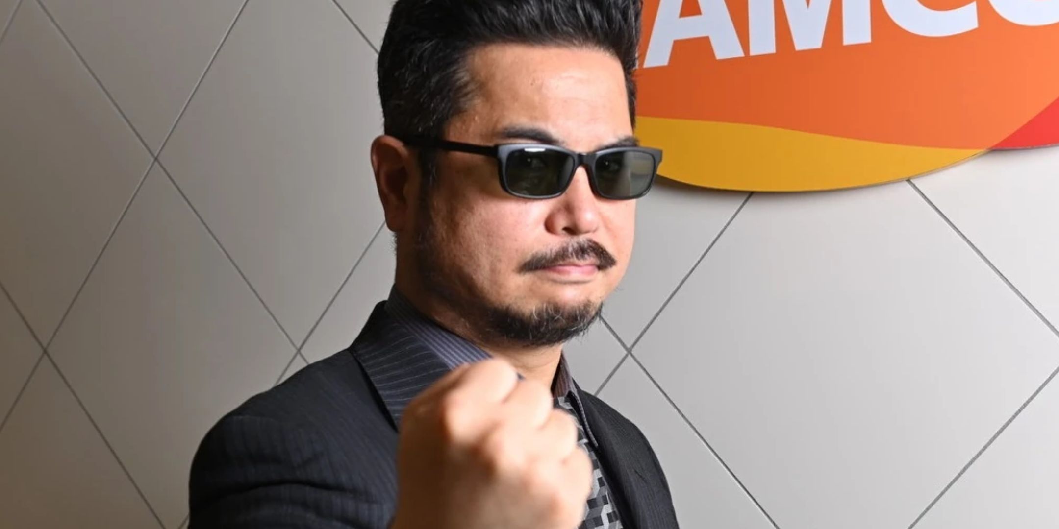 Katsuhiro Harada wearing sunglasses and putting a fist to the camera