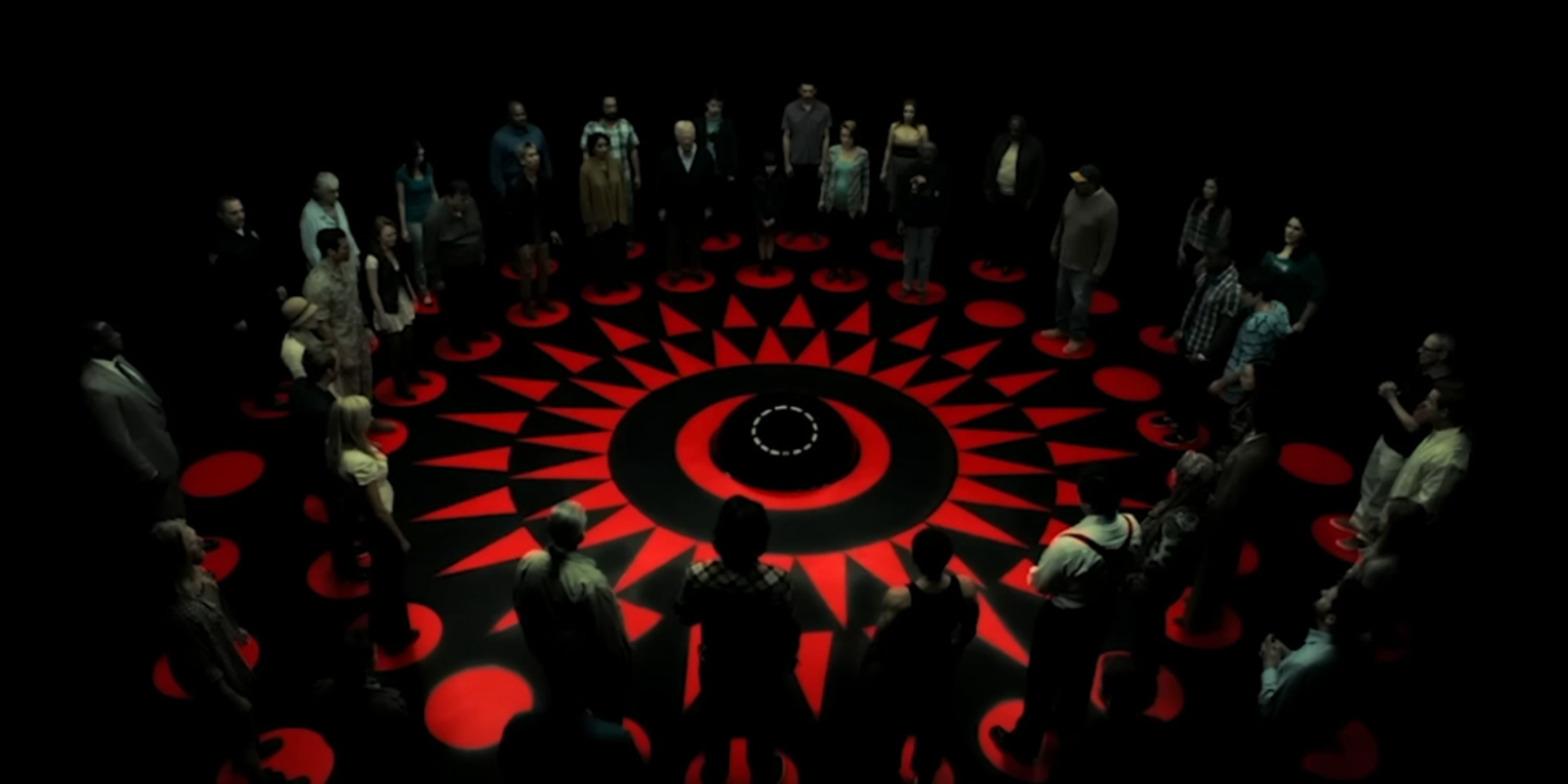 The contestants stand around a circle in a dark room.