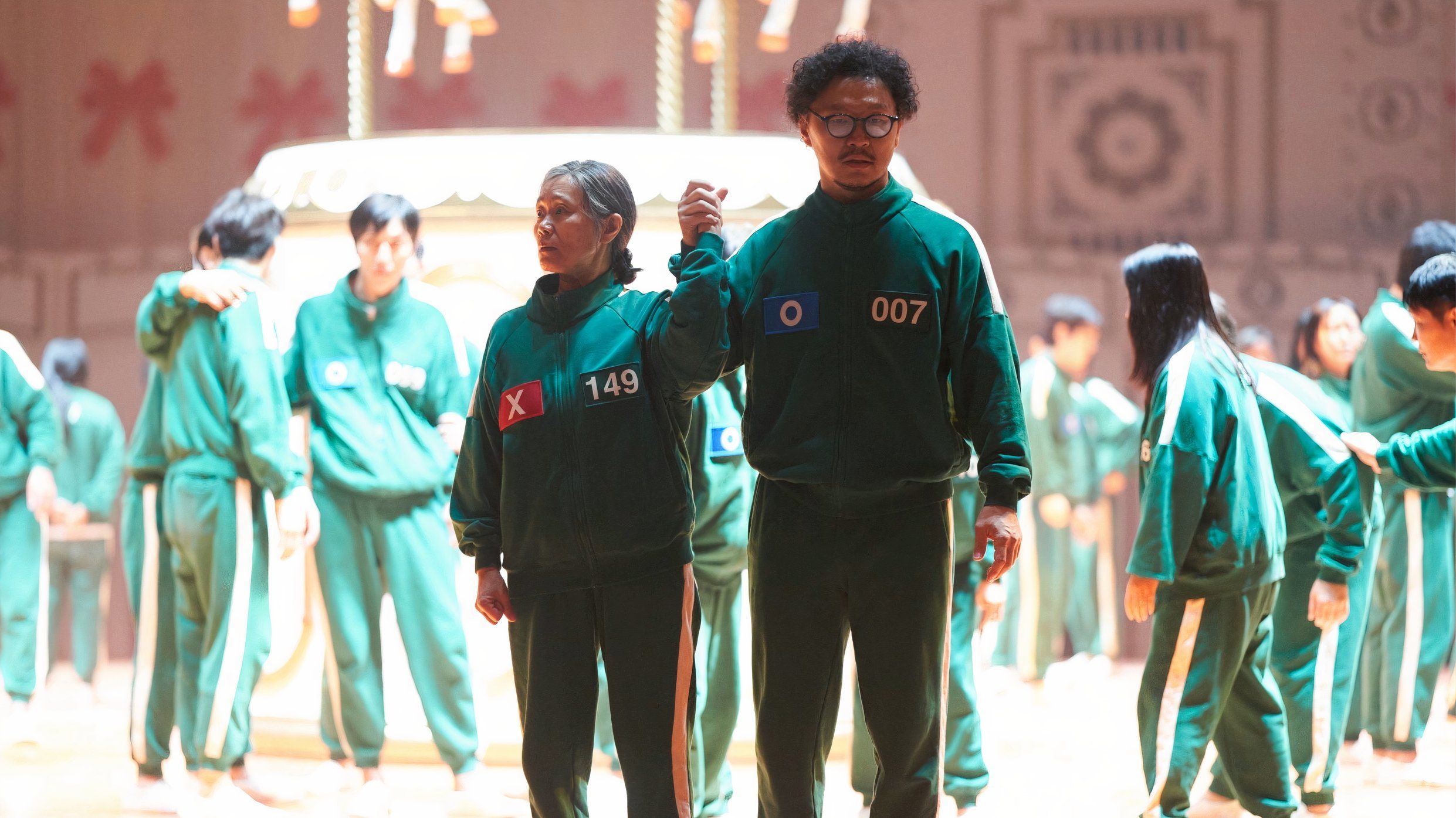 Jang Geum-ja and Park Yong-sik in Squid Game Season 2 standing  holding hands.