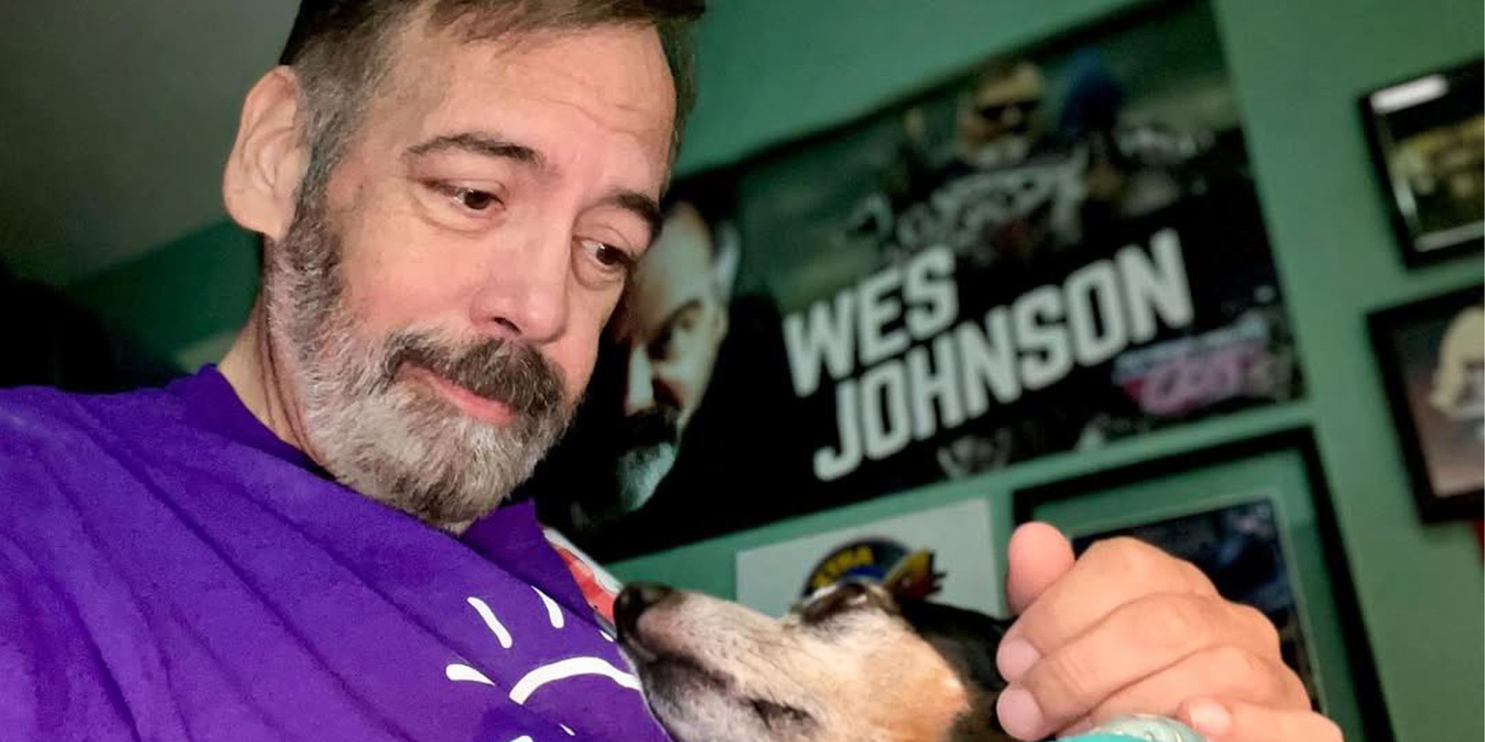 Wes Johnson petting his dog in front of a poster with his name written on it.