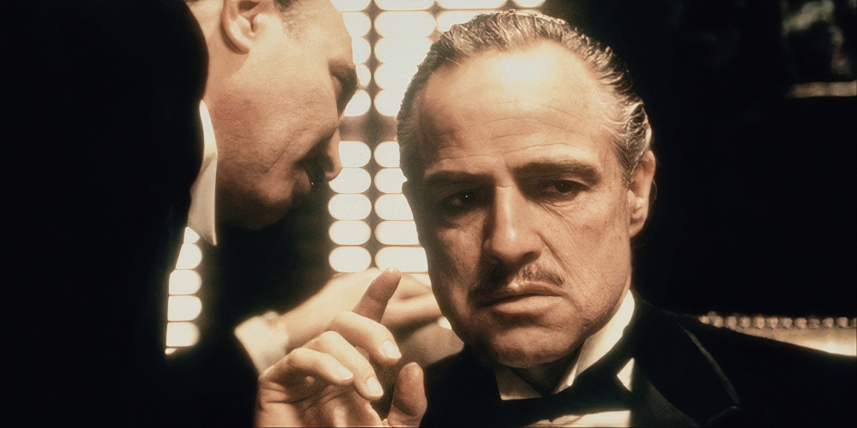 A close-up of Marlon Brando as Vito Corleone with another character speaking into his ear in The Godfather.