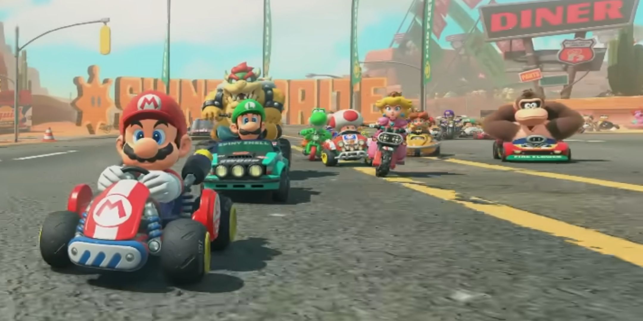 Mario and other characters including new Donkey Kong driving along a dusty desert road by a diner in the reveal for Mario Kart 9.