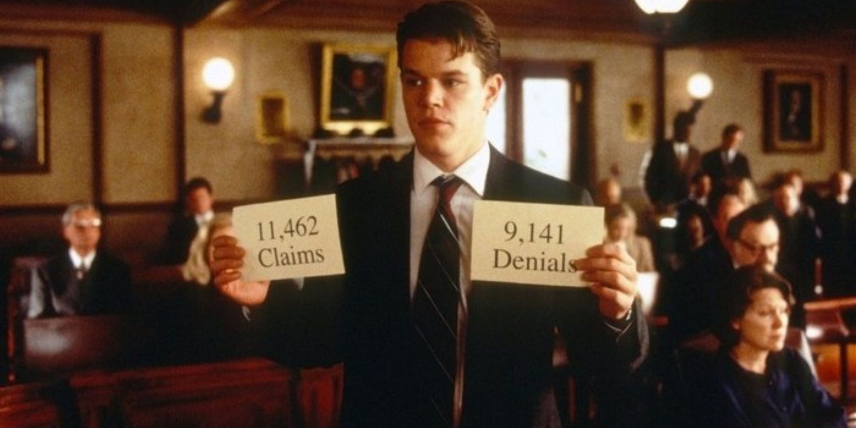 Matt Damon holding up cards with the number of insurance claims and denials in court in The Rainmaker.