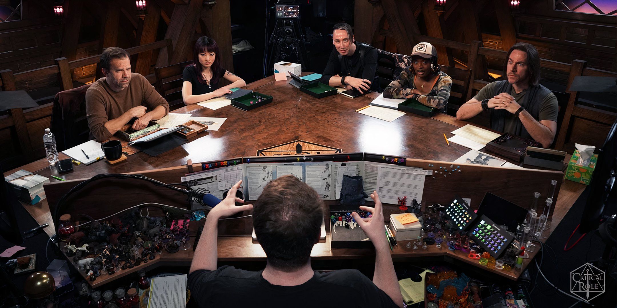 Liam O'Brien, Jasmine Don, Alex Ward, Celia Rose Gooding, Brennan Lee Mulligan, and Matthew Mercer sitting around the Critical Role Table.