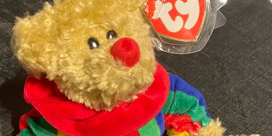A brown teddy in a multicolor clown costume sits on a couch