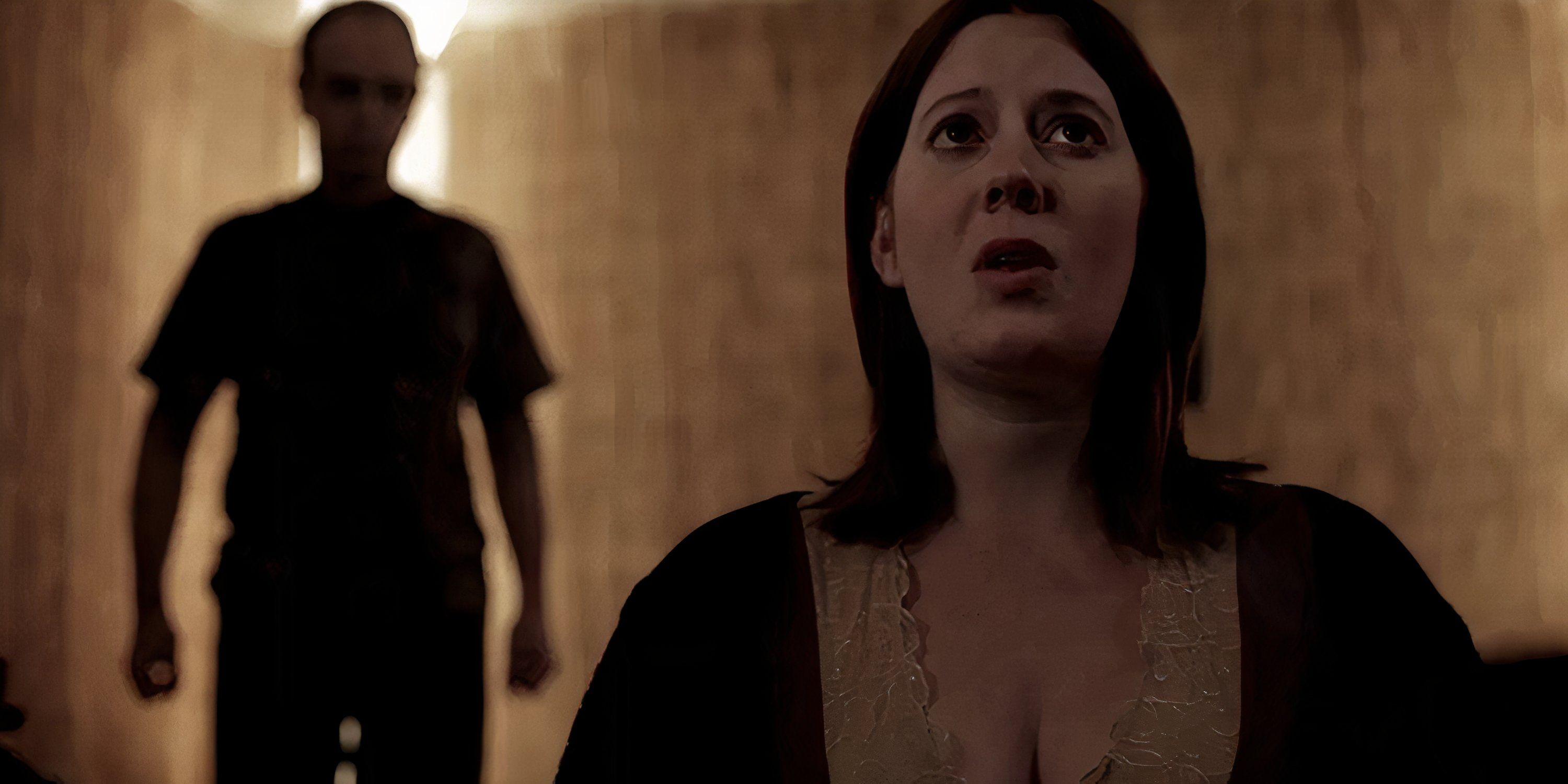Tricia looks up while a man stands behind her in Absentia.