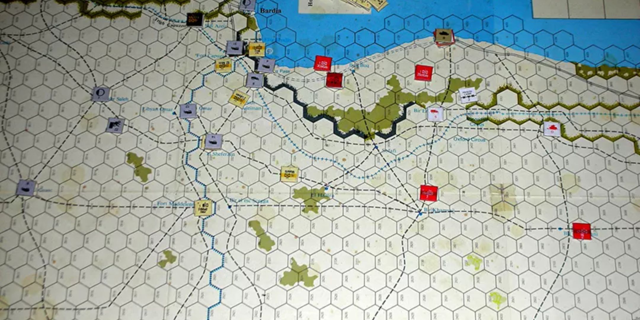 A map of the Campaign for North Africa board game with various units on the board by the coast.