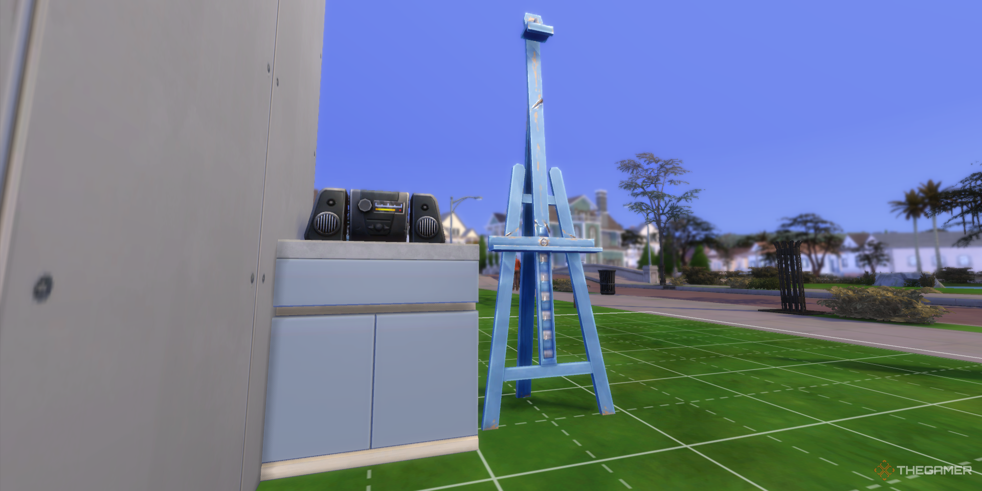 A counter with a radio and a blue easel are on the front lawn of an unfinished building in The Sims 4.