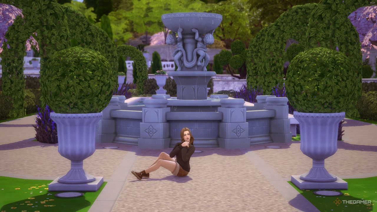 A female Sim sits and poses by a fountain