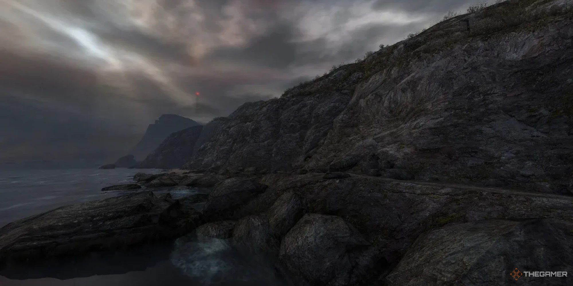 A screenshot from Dear Esther. A rugged coastline with a faint red light visible in the misty distance.