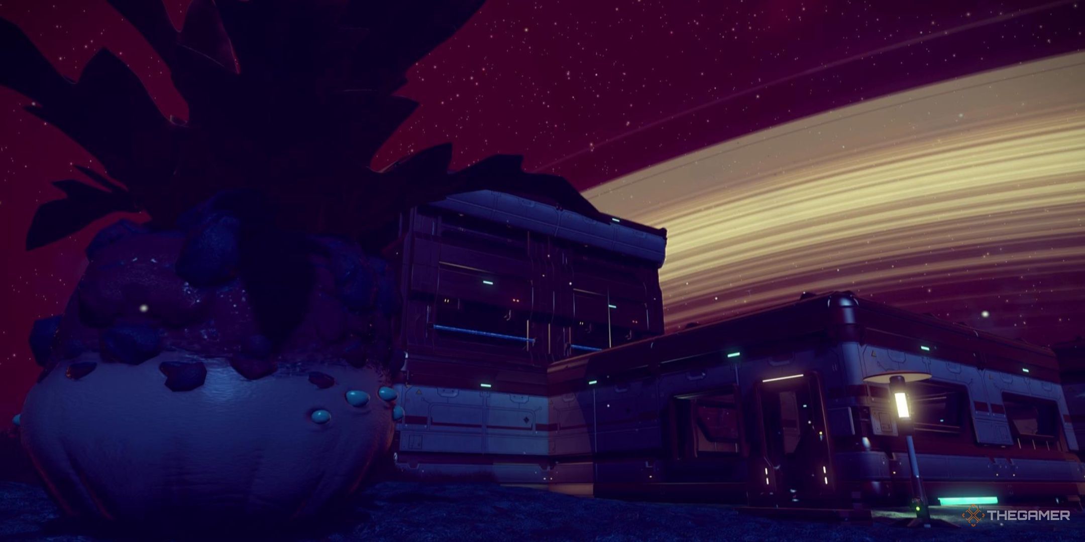 A plant-like creature stands on the left, a base sits in the center, with the ring of the planet wrapping across the sky, all in No Man&rsquo;s Sky.