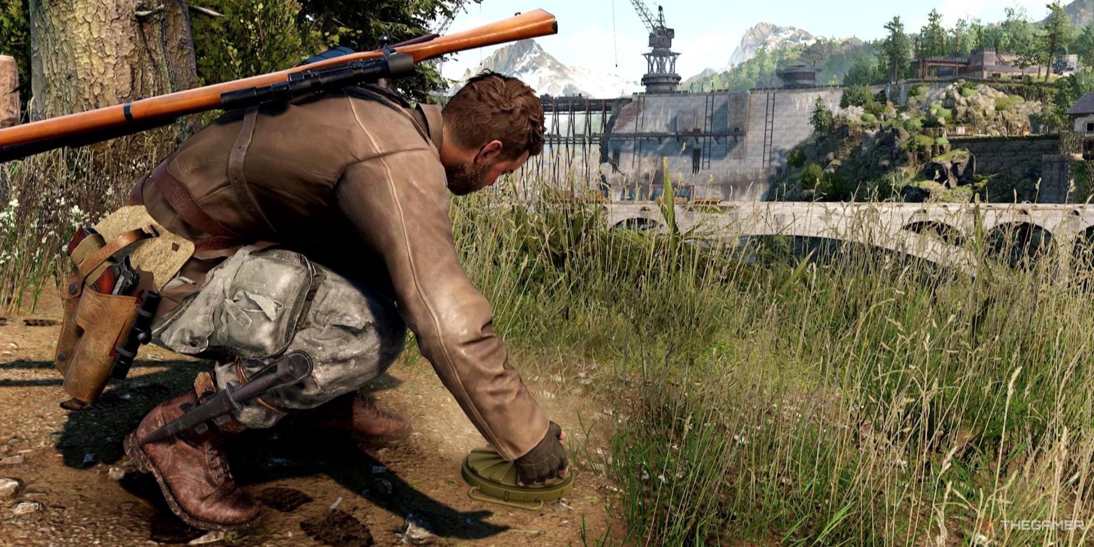 Harry lies a mine on the ground in Sniper Elite: Resistance, with a damaged dam in the background.