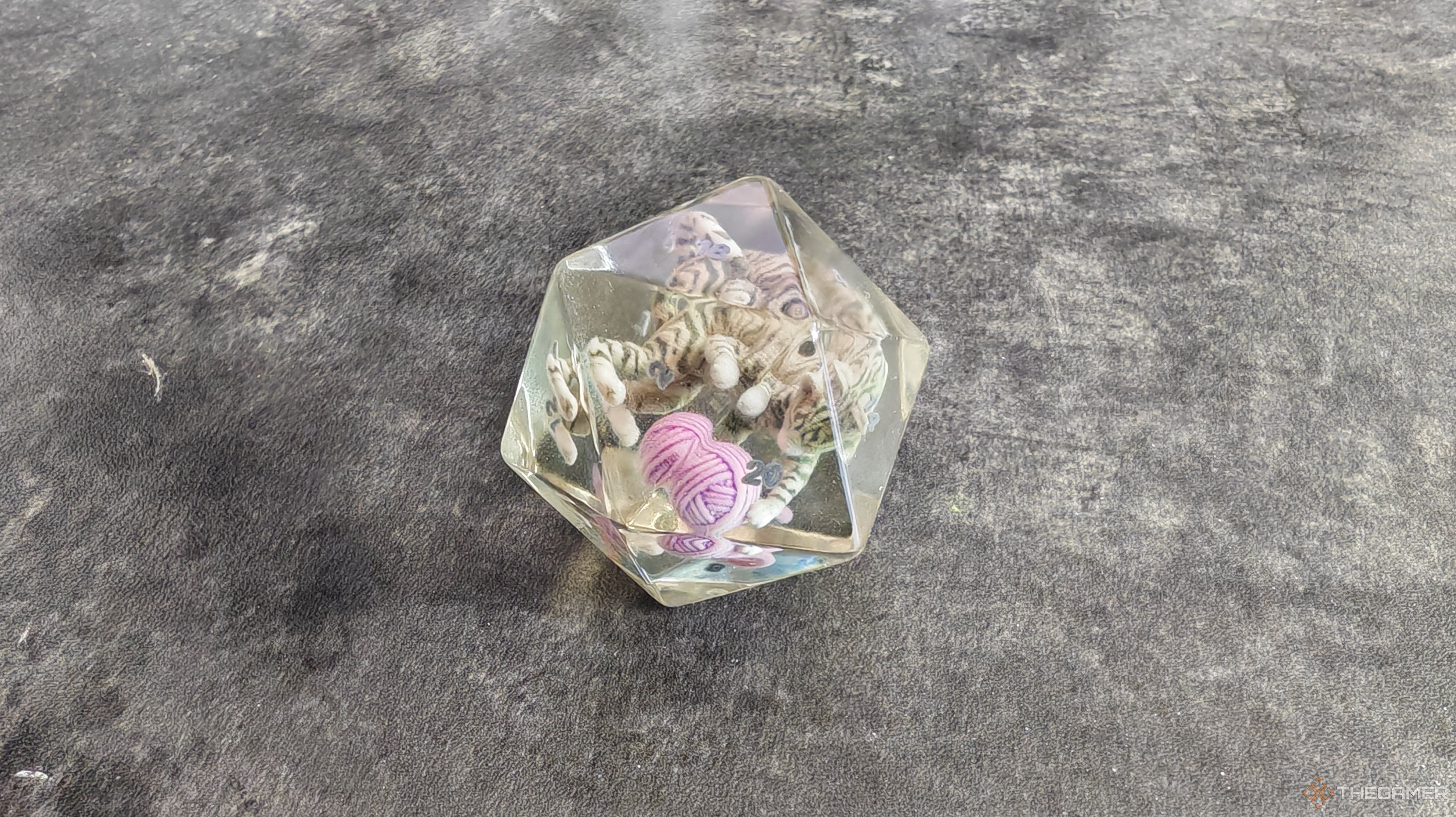 A d20 die made of clear resin with a cat inside playing with a ball of yarn