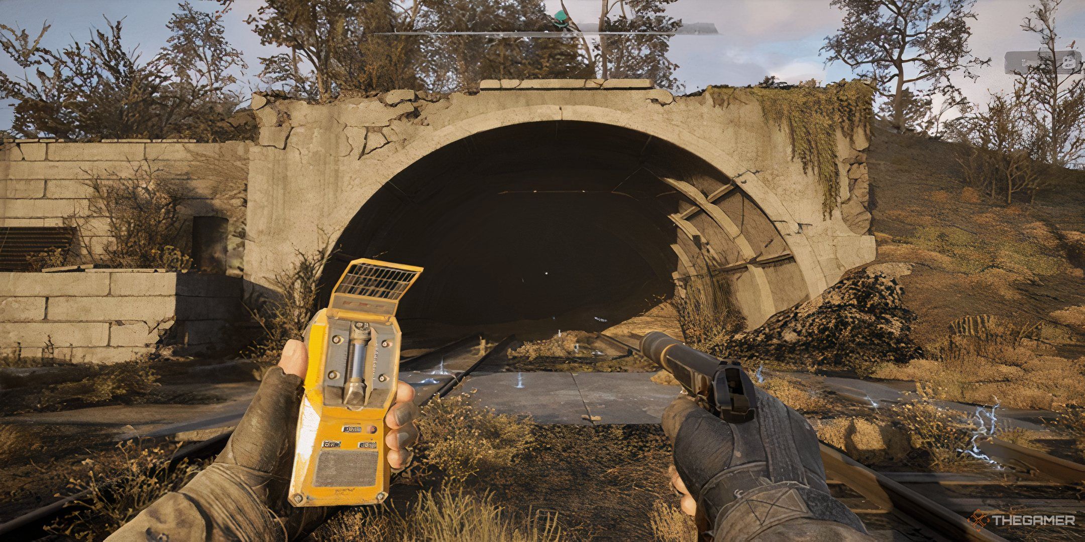 Player with a gun in one hand and a device in the other, looking at a tunnel in Stalker 2 Heart Of Chronobyl.