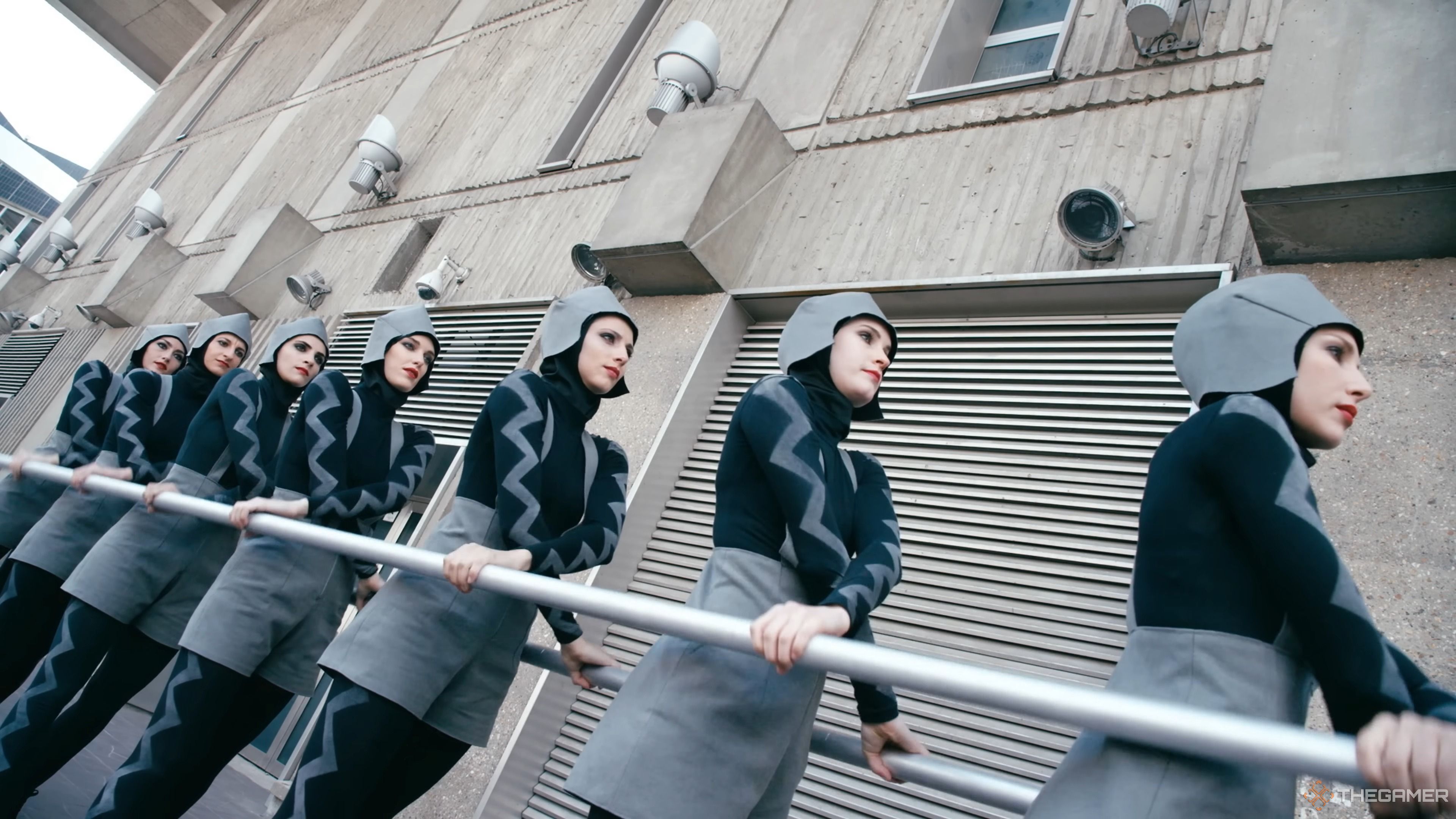 Go! by the Chemical Brothers, showing women wearing odd grey costumes holding a bar.